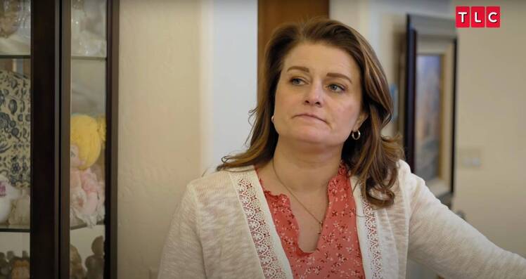 Robyn Brown wearing a coral blouse and cream cardigan, looking serious during a scene from Sister Wives.
